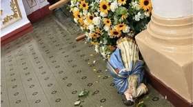 Imagem de Nossa Senhora do Rosário caída no chão de uma igreja, ao lado de um andor com flores, após ser derrubada e danificada